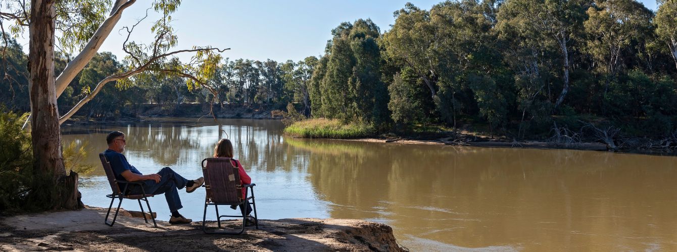 Two people sitting in deck chairs alongside the river